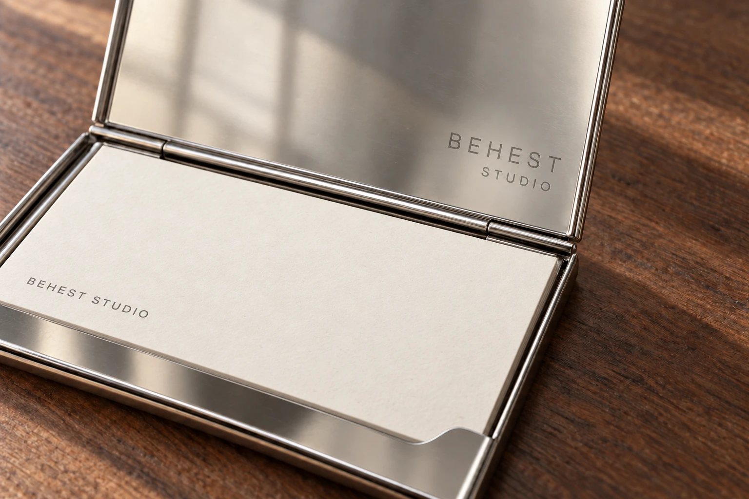 Open card case on a walnut desk holding a business card, engraving inside the lid. Design concept.