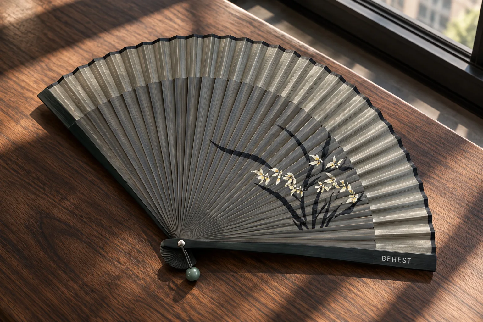 Open folding fan with a painted orchid on a walnut table.